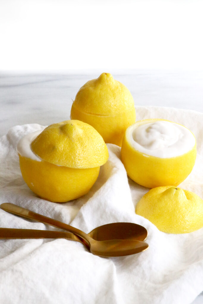 Three lemons with tops cut off and filled with coconut cream. Sitting on white napkins with two spoons at the bottom of photo.