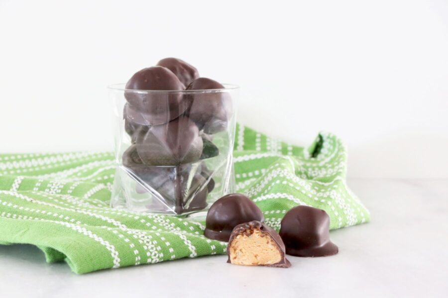 Glass filled with chocolate covered peanut butter balls. Sitting on top of green towel. A few of the holiday balls are on the bottom of photo.