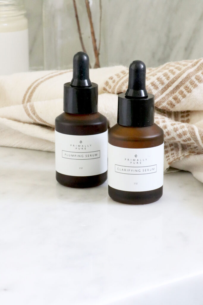 two bottles of Primally Pure serum on counter top with towel in the background.