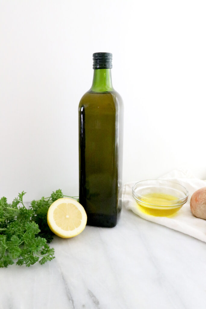 Bottle of olive oil with sliced lemon and parsley on the left and small bowl of olive oil on the right.