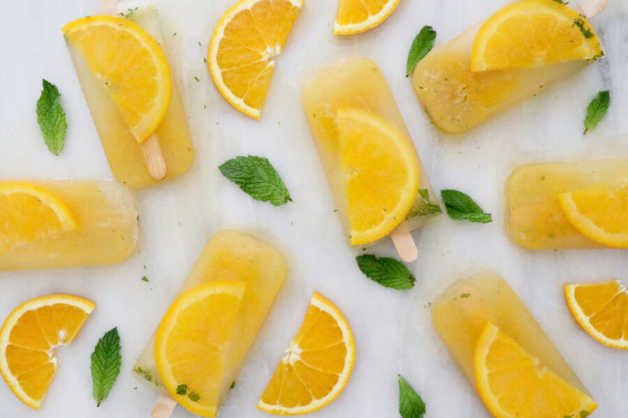 Popsicles with orange slices and mint spread throughout photo.