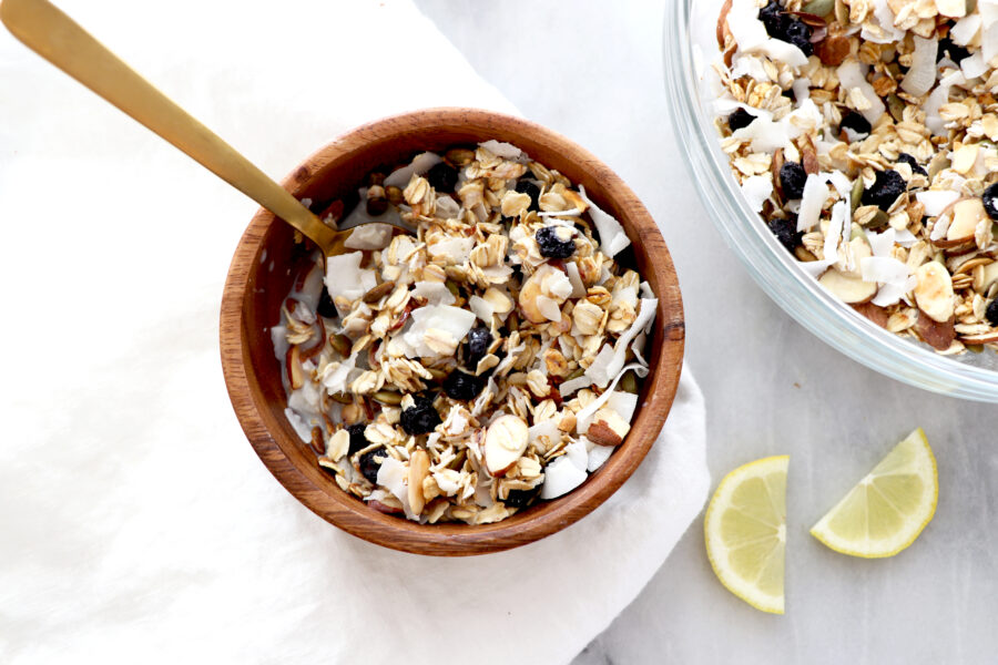 wooden bowl filled with muesli that containers oats, blueberries, shredded coconut pumpkin seeds, almonds and lemon.