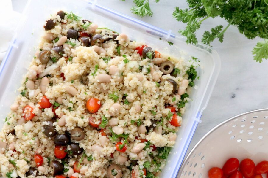 Tupperware filled with quinoa salad with tomatoes and parsley around container.