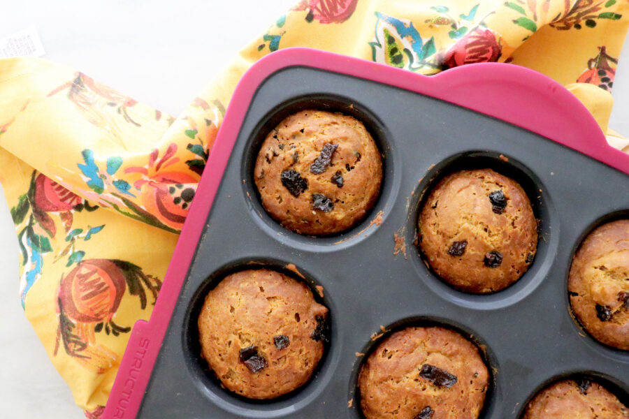 Muffin tin filled with gingerbread prune muffins all on a floral napkin and diced prunes on the side.