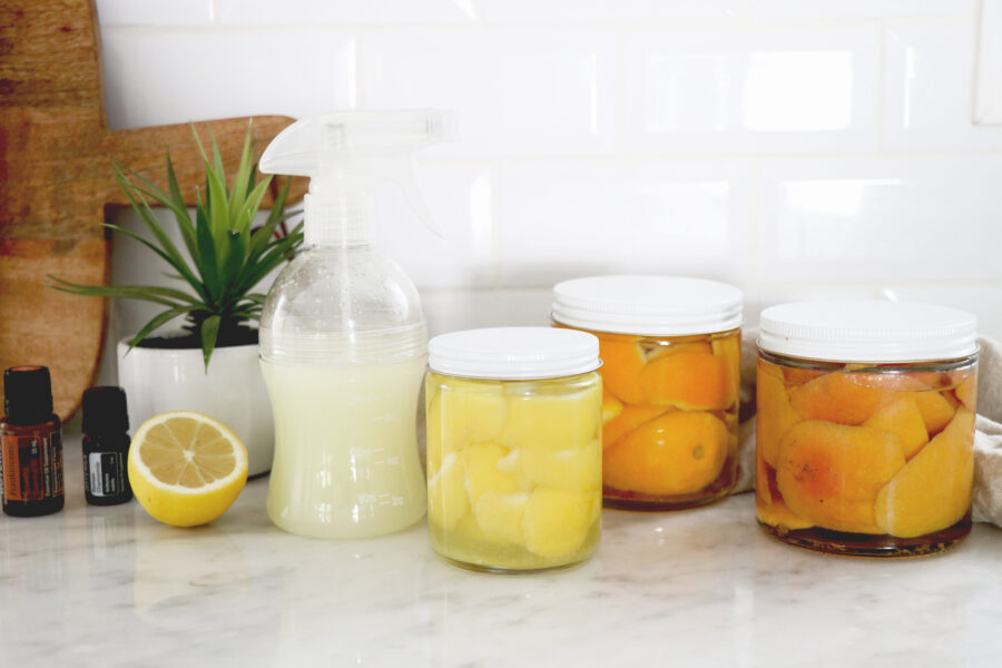 3 clear jars with citrus cleaner and one spray bottle all on countertop.