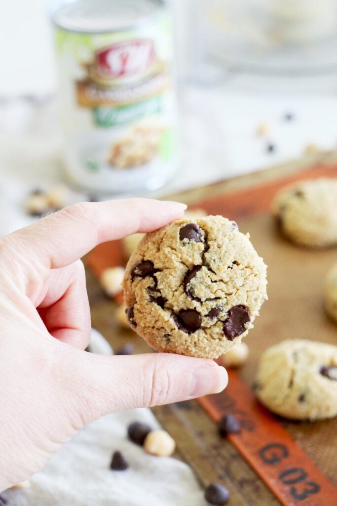 Hand holding chickpea chocolate chip cookie over baking sheet of cookies.