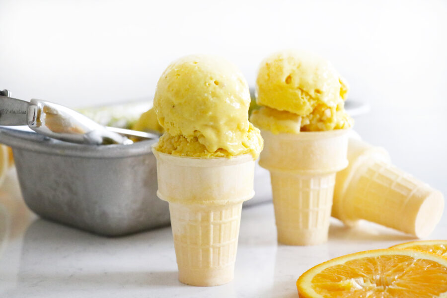 Two ice cream cones with a scoop of orange nice-cream. 