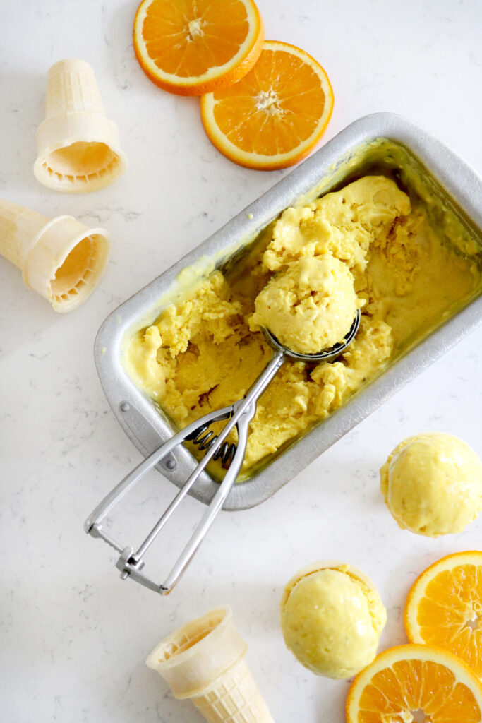 Ice cream pan with scooper filled with orange nice-cream.