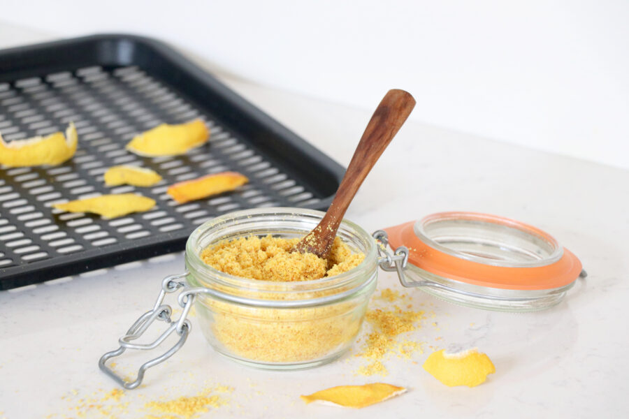 Glass container with citrus peel powder and dried peels in the background.