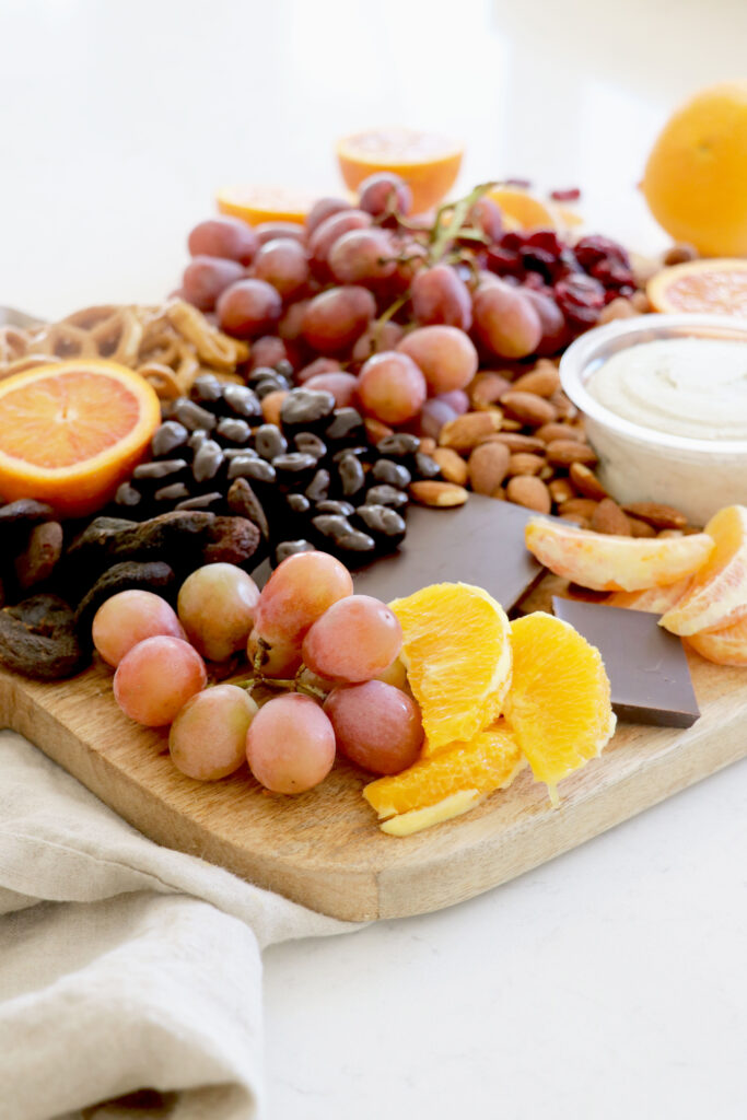 Snack board with grapes, citrus, raisins, chocolate and vegan cheese.