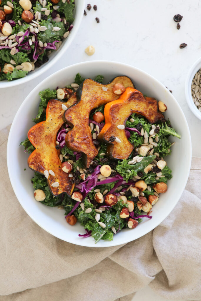White bowls with kale salad and roasted acorn squash on tan napkins.
