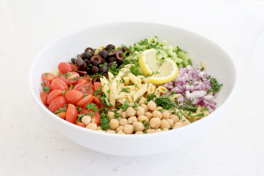 Large white bowl with pasta salad topped with veggies.