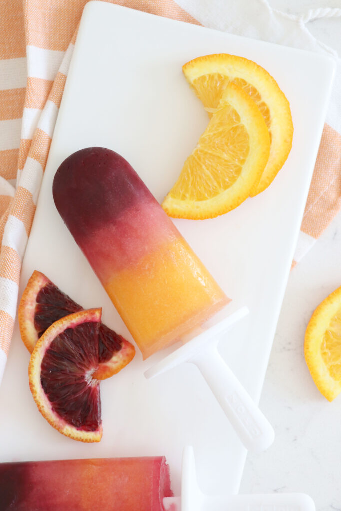 One citrus popsicle with sliced citrus on white plate.