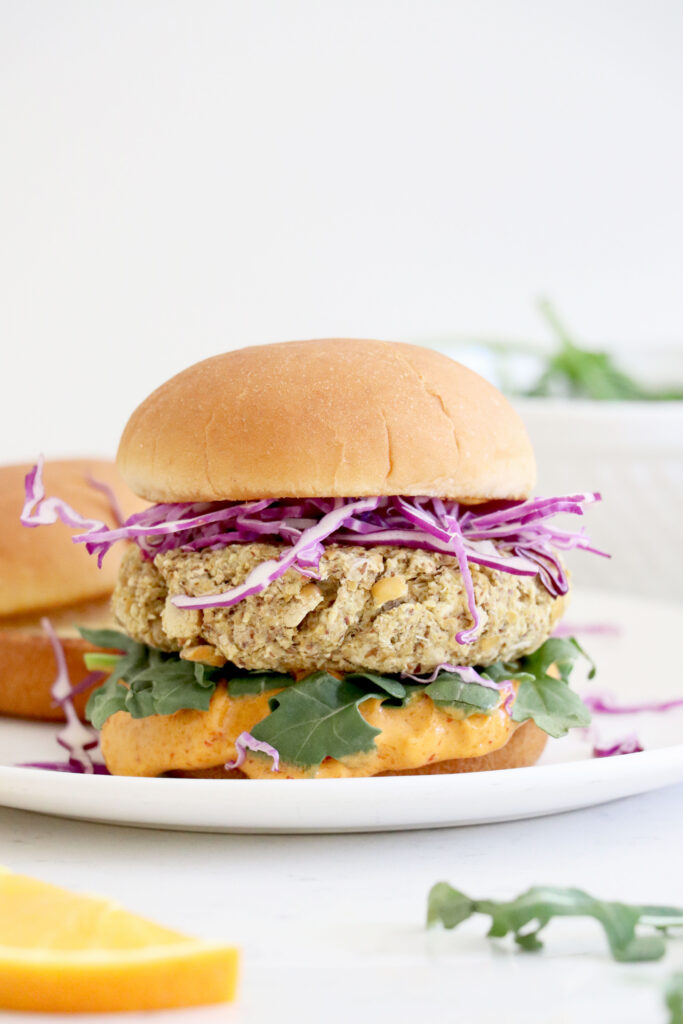 White plate topped with chickpea burger, cabbage, arugula and bun.