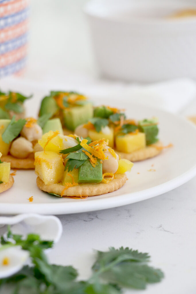 Plate of chickpea salad bites on crackers and cilantro in the front of picture.