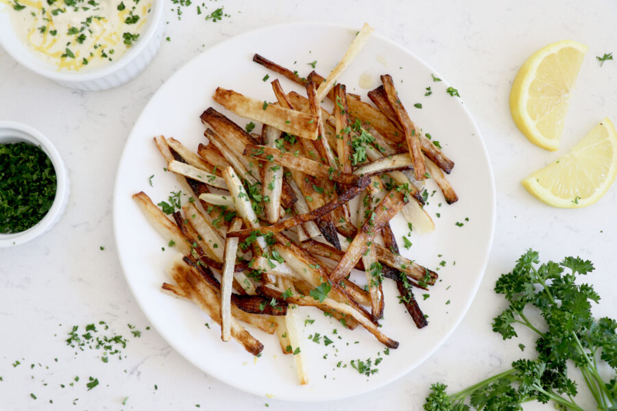 White plate topped with parsnip fries and an aioli dipping sauce.