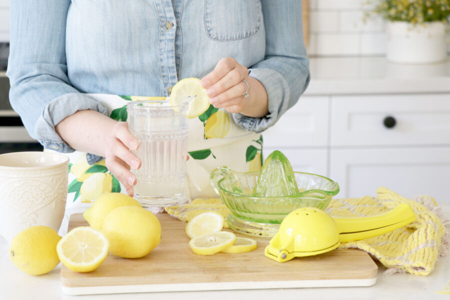 Megan adding lemon slice into glass of water with lemons around cutting board.