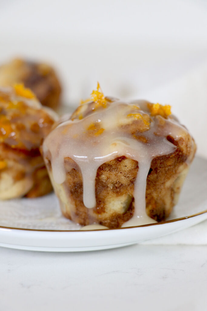Plate with cinnamon roll muffin topped with icing and orange zest.