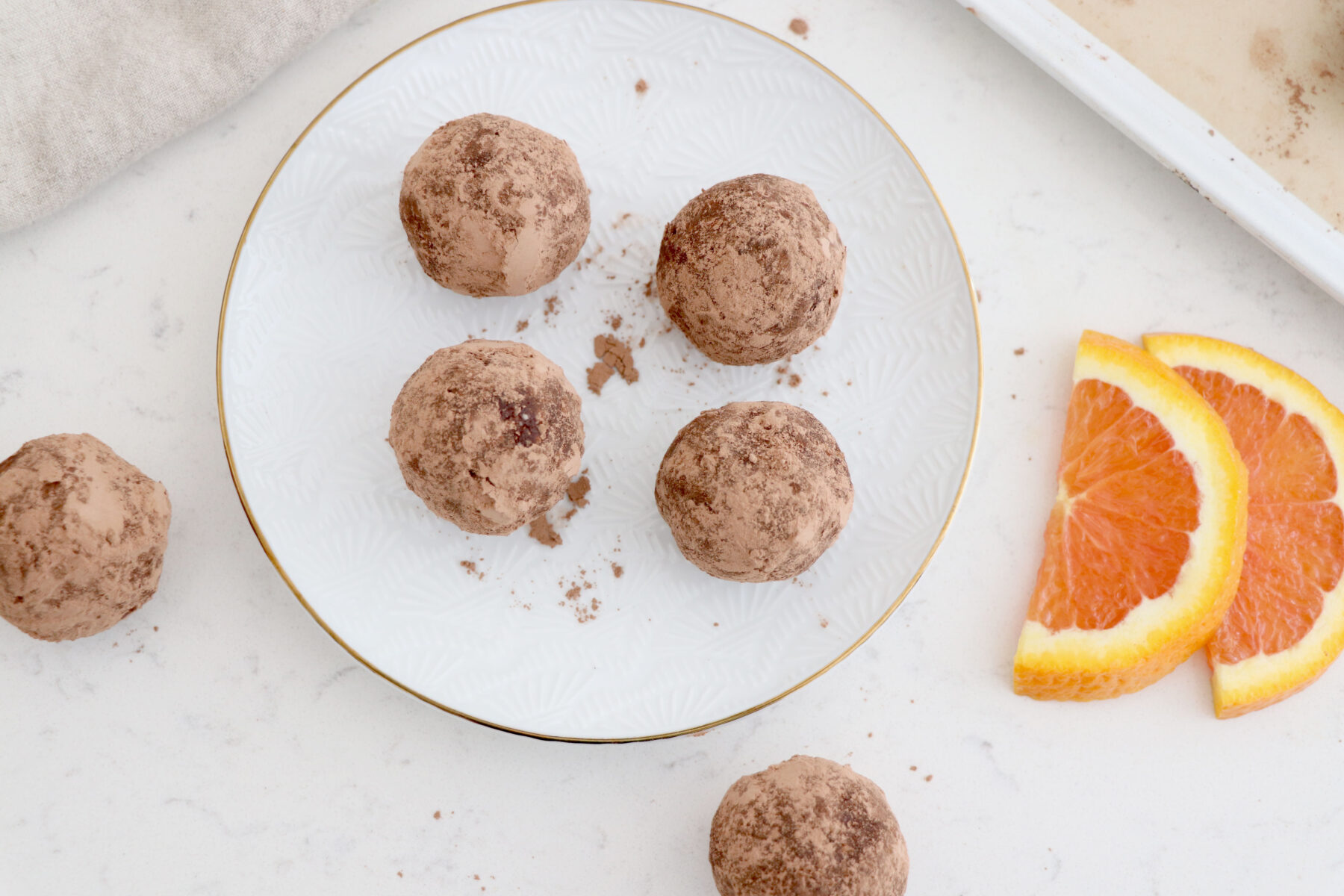 White plate of 4 chocolate truffles with 2 on each side and 2 orange slices on right side.