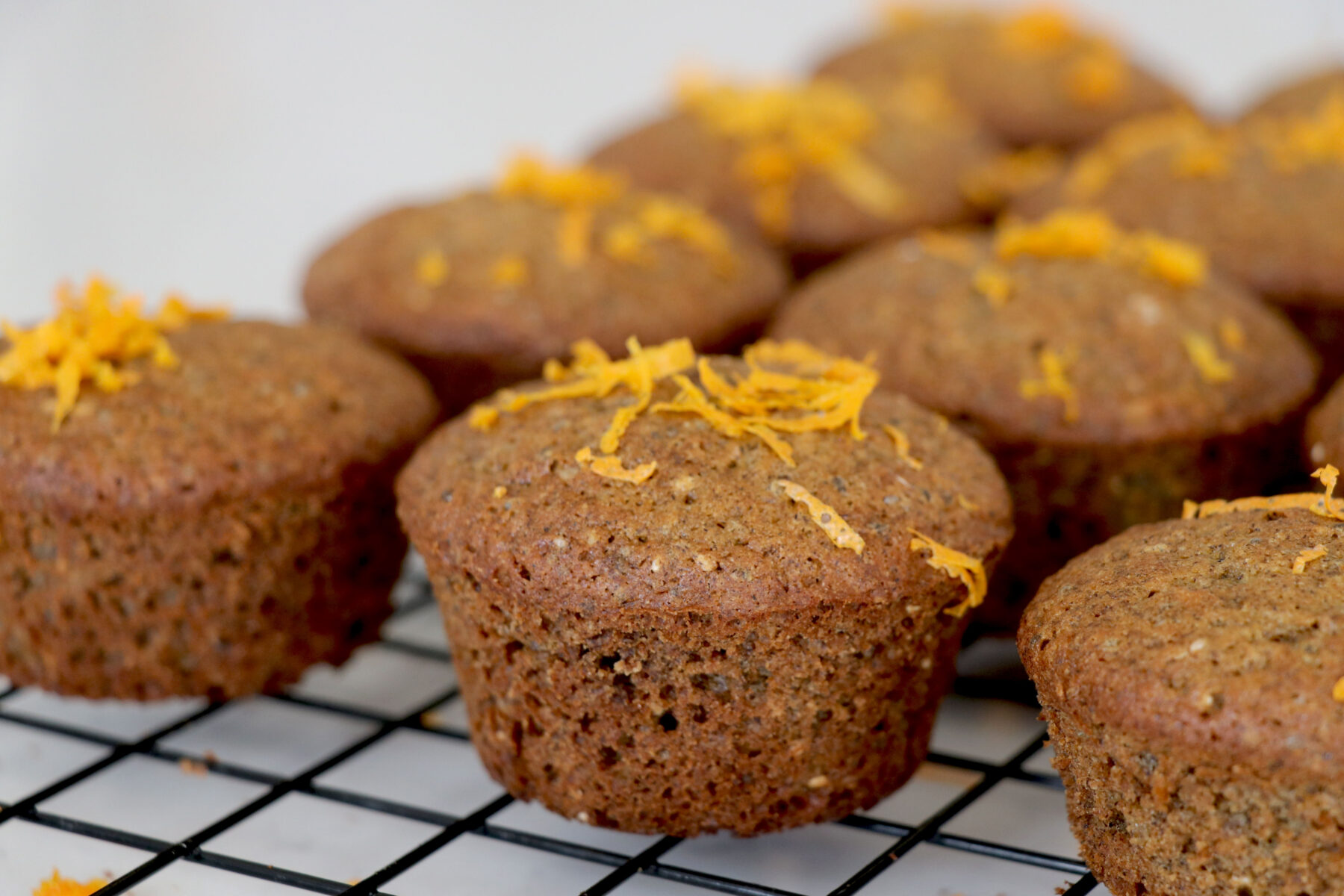 Chia muffins on a wire rack with orange zest on top.