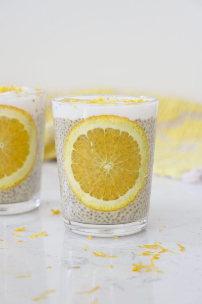 Glass with orange chia pudding, whipped topping on top and orange slice on side of glass.