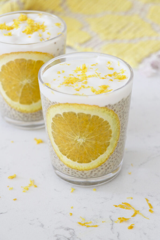 Two glass jars with orange chia pudding with cream and orange zest on top.