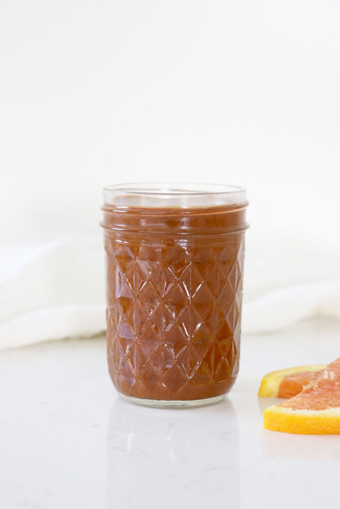 Glass jar with bbq sauce and orange slice on the side.