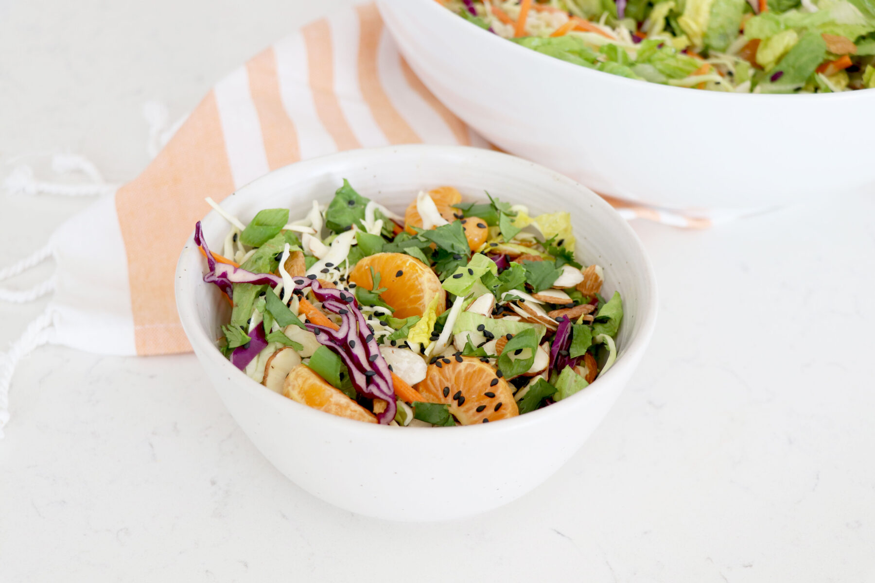 White bowl with sesame salad topped with mandarin oranges.