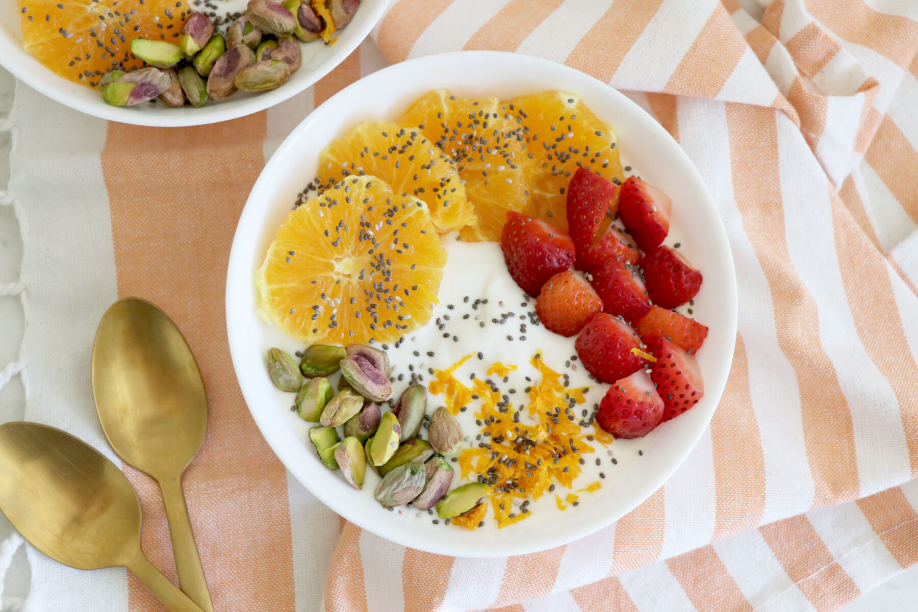 White bowl with yogurt, sliced fruit and pistachios on top.