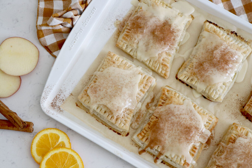 Apple pop tarts with icing on top on a white baking sheet.