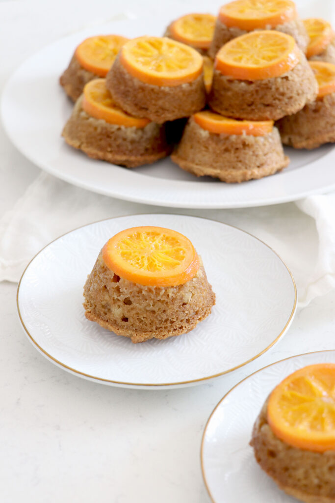 Upside down orange mini cake on plate, with more piled in background